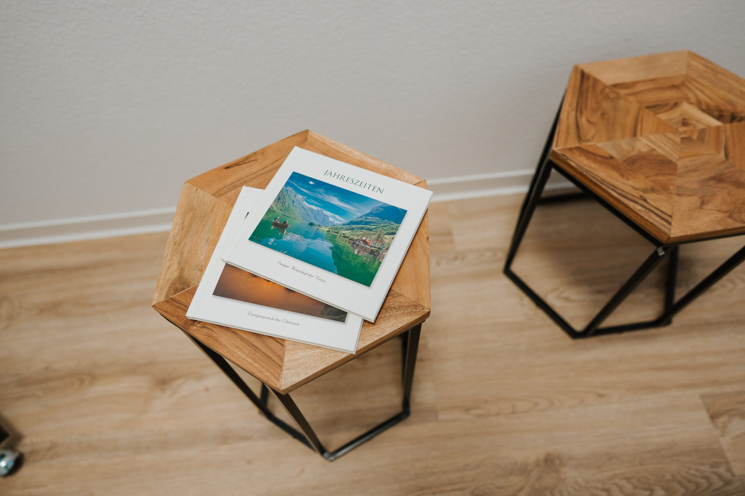 Auf einem sechseckigen hölzernen Beistelltisch mit schwarzem Metallrahmen, der vielleicht in einem Büro der Neurologe Wolfenbüttel steht, liegen zwei kleine Broschüren mit Landschaftsfotos auf dem Umschlag. Der Tisch steht auf einem hellen Holzboden neben einem ähnlichen Tisch.