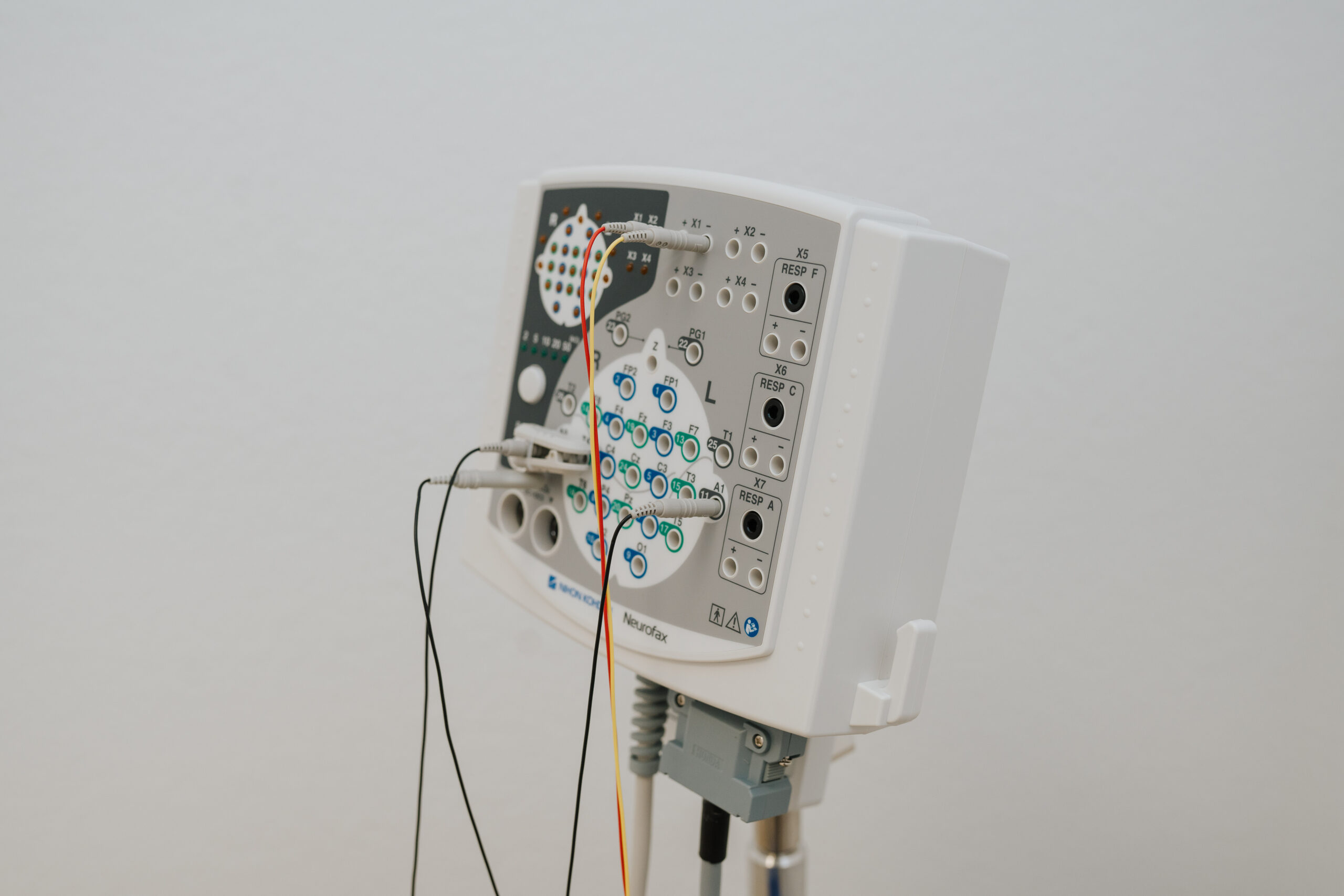 Eine Nahaufnahme eines medizinischen Neurofeedback-Geräts aus Wolfenbüttel mit mehreren Tasten, Anzeigeleuchten, angeschlossenen Kabeln und Eingangsanschlüssen vor einem schlichten weißen Hintergrund.