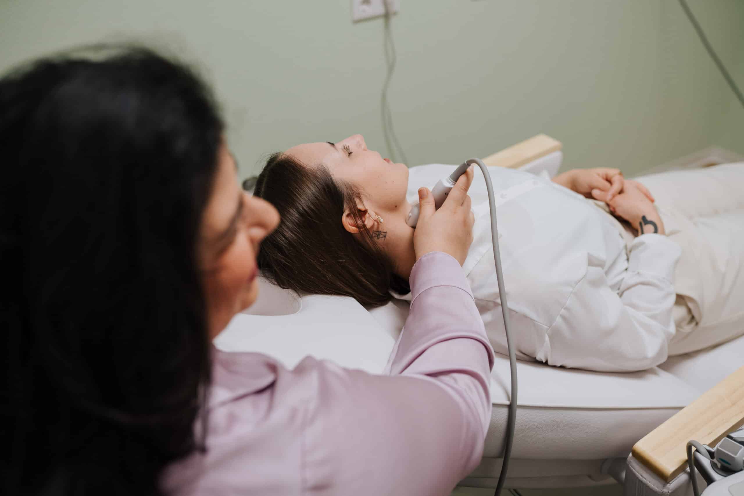 Eine medizinische Fachkraft hält ein Ultraschallgerät an den Hals eines auf einem Untersuchungstisch liegenden Patienten und führt in einer Klinik neurologische Diagnostik Wolfenbüttel durch.