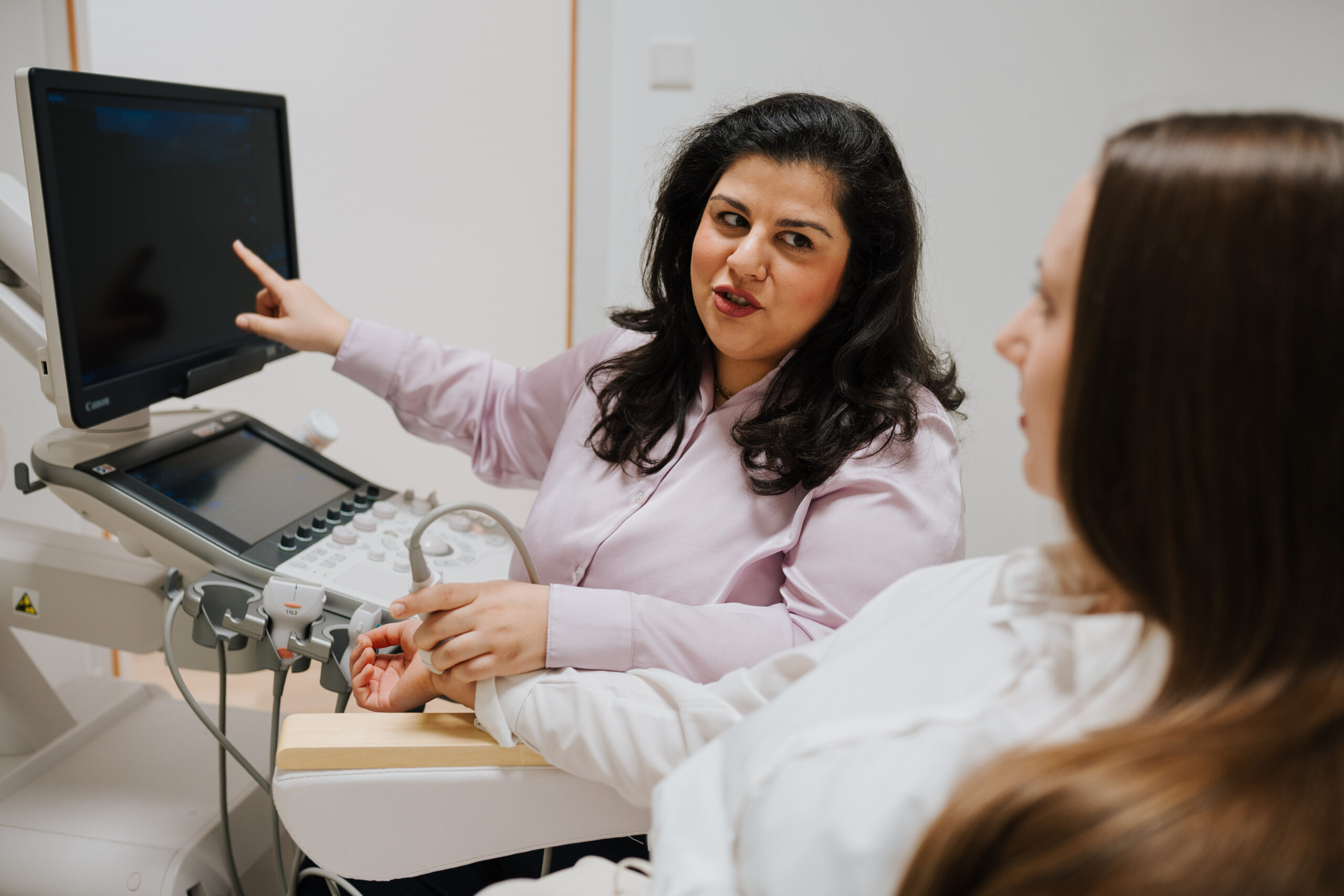 Eine medizinische Fachkraft in der Neurologischen Praxis Wolfenbüttel erklärt einem Patienten während einer medizinischen Beratung Informationen auf einem Ultraschallmonitor. Der Patient sitzt und hört aufmerksam zu.