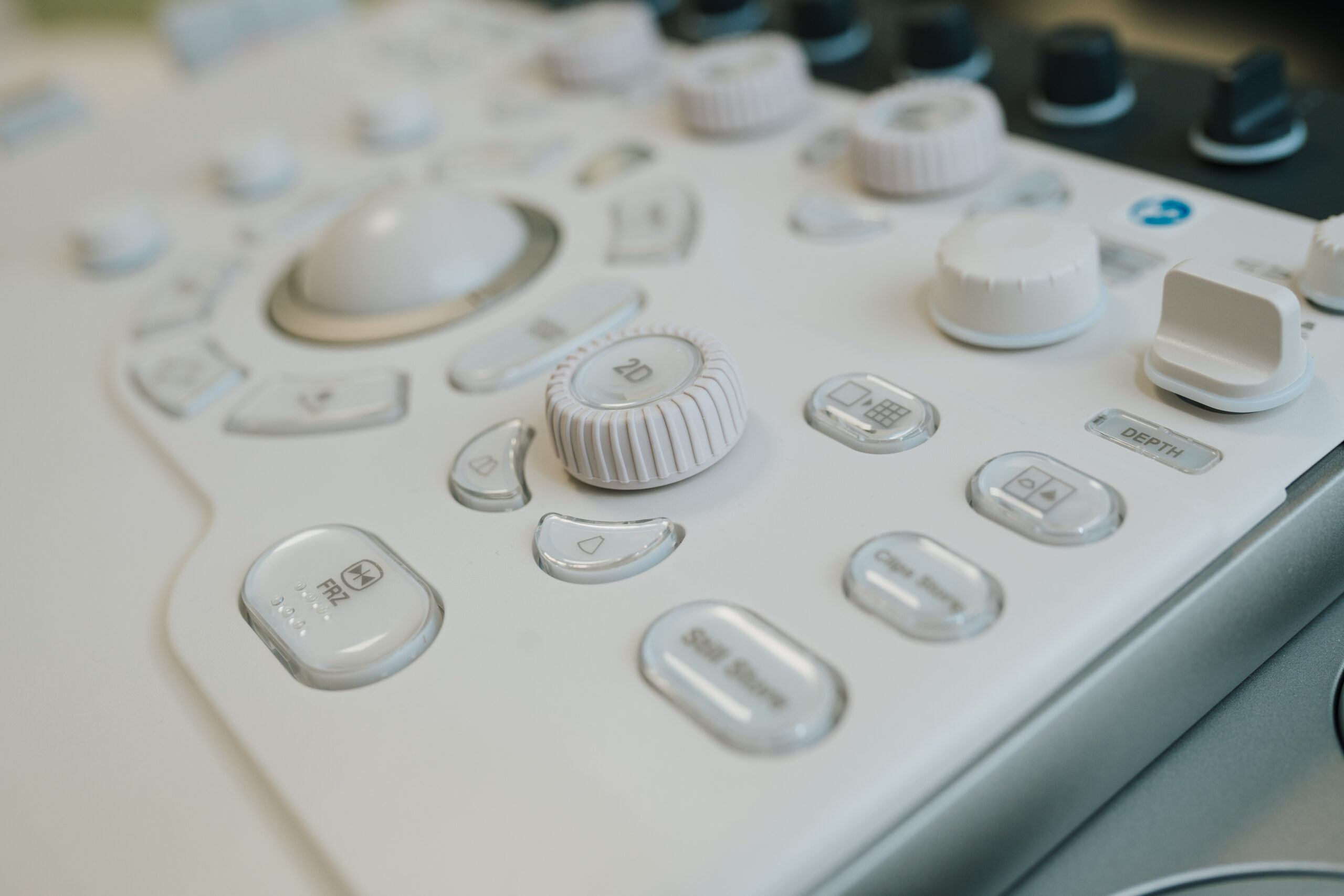 Nahaufnahme eines weißen Bedienfelds mit mehreren Einstellrädern, Knöpfen und Reglern, von denen einige mit Symbolen und Text wie "2D" und "DEPTH" beschriftet sind, wahrscheinlich von einem in der Neurologischen Diagnostik Wolfenbüttel verwendeten medizinischen Gerät.